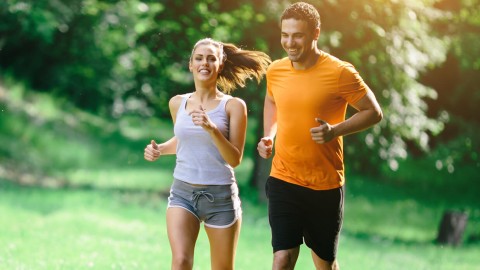 Ein Paar joggt durch einen Park. Der Hintergrund ist grün und verschwommen.