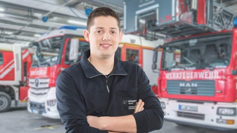 Ein junger Mann mit verschränkten Armen steht vor zwei Feuerwehrfahrzeugen in einer Garage.